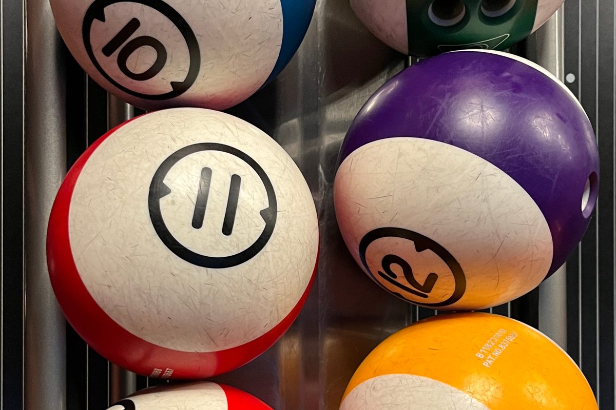 House bowling balls with finger holes on a rack, sorted by weight as in this bowling ball weight guide